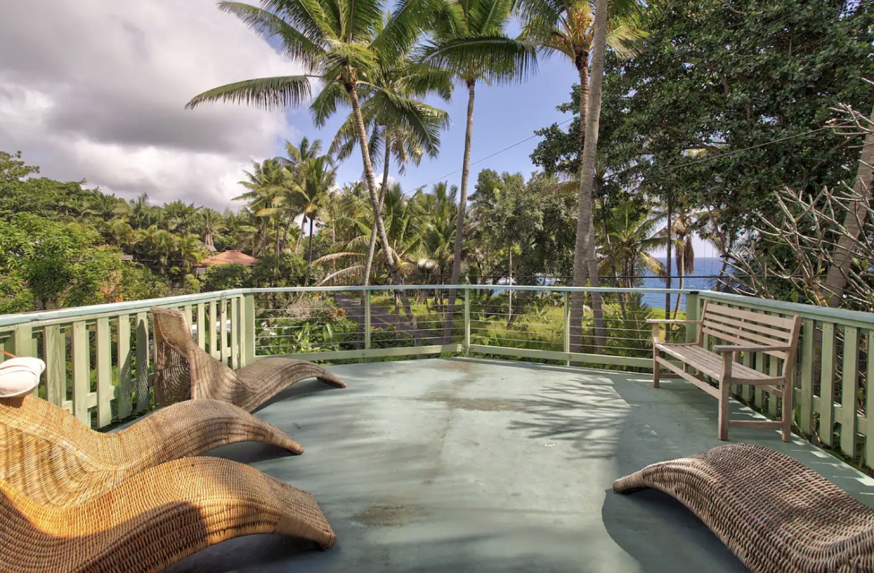 Ocean-view deck with wicker loungers framed by coconut palms
