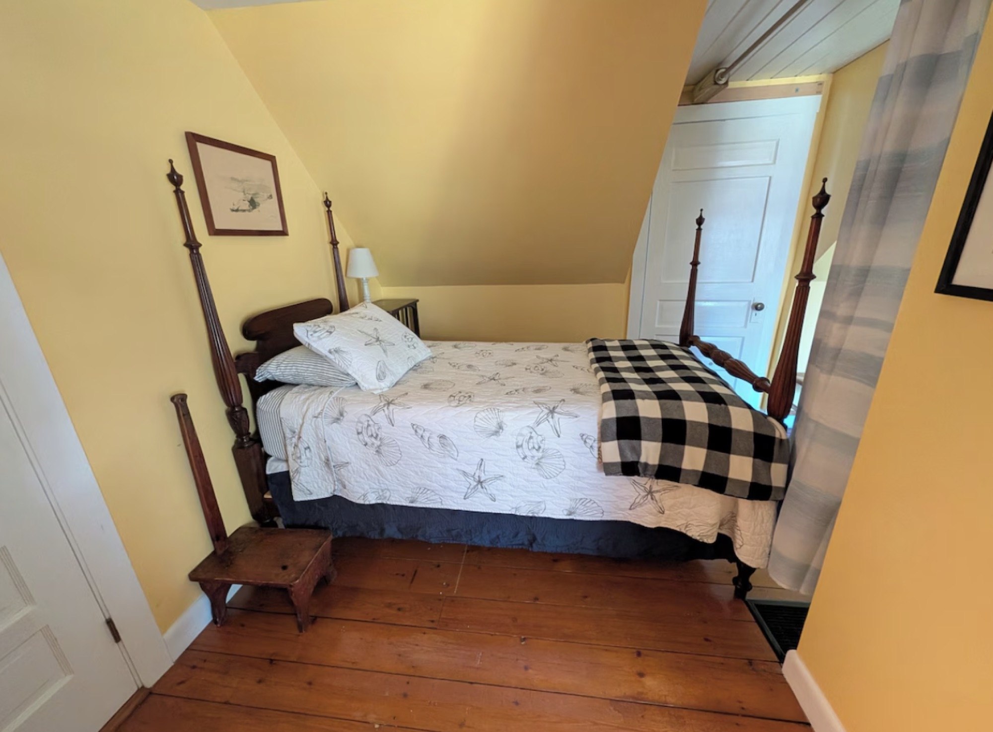 A yellow attic bedroom with a four-poster bed and wide pine floorboards