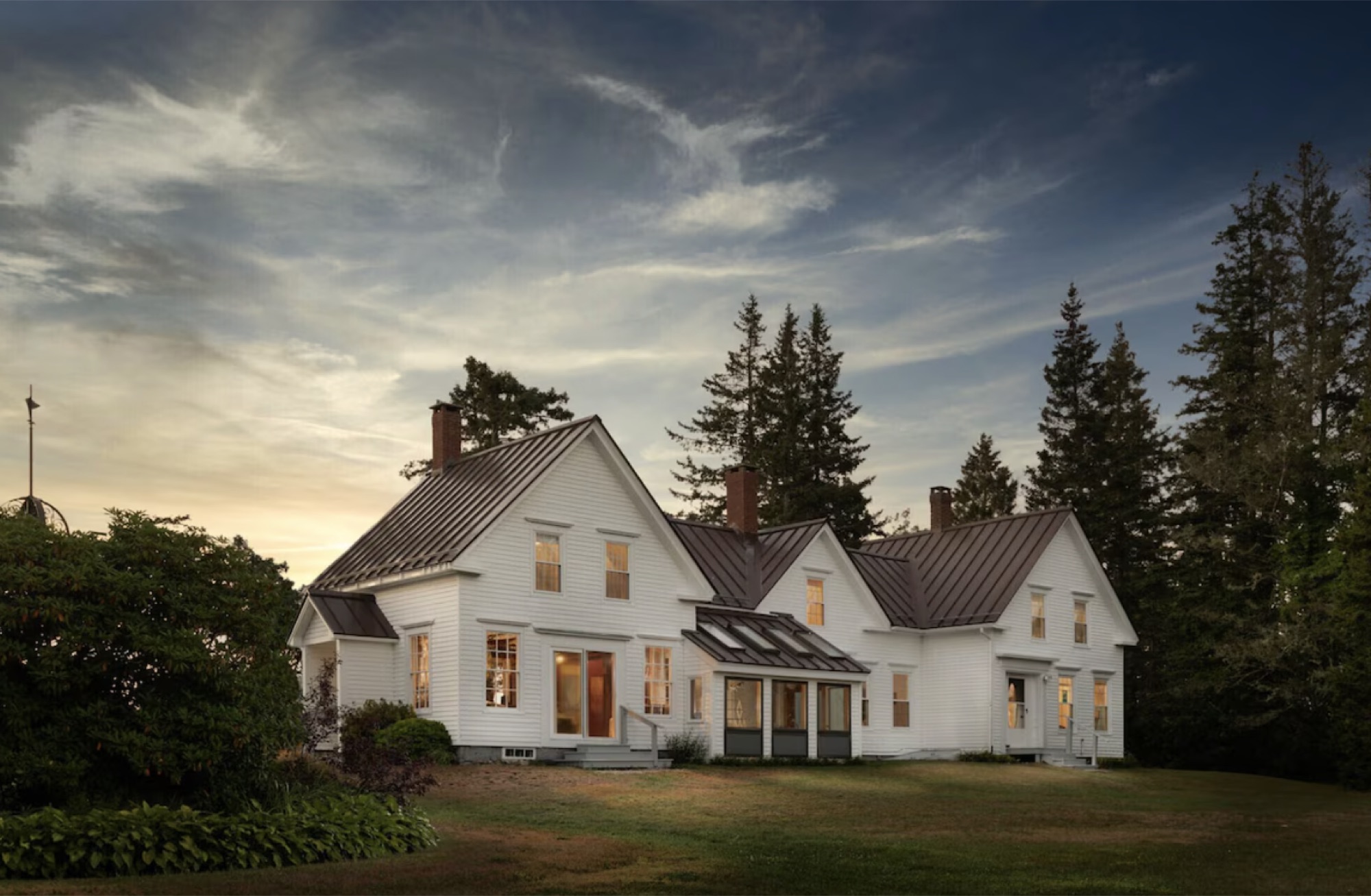 The white clapboard retreat house at dusk with warm light in the windows