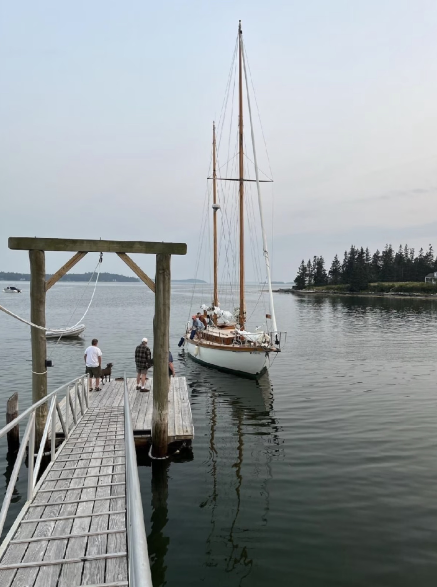 A wooden sailing boat tied alongside the dock on a calm Maine morning