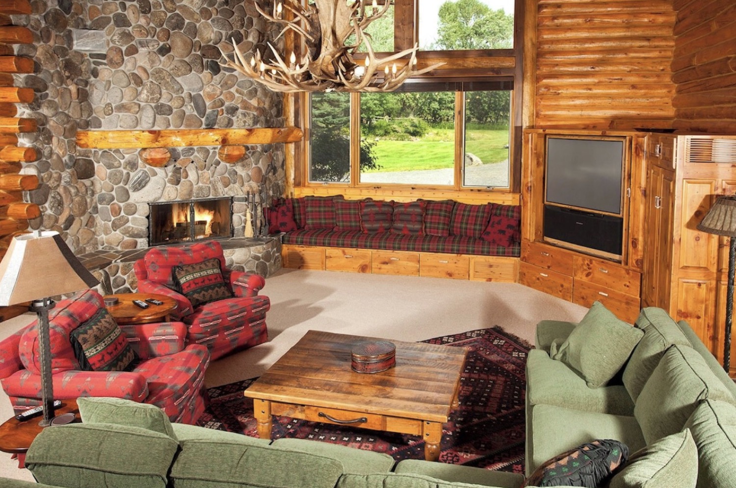 A lodge living room with a stone fireplace and antler chandelier