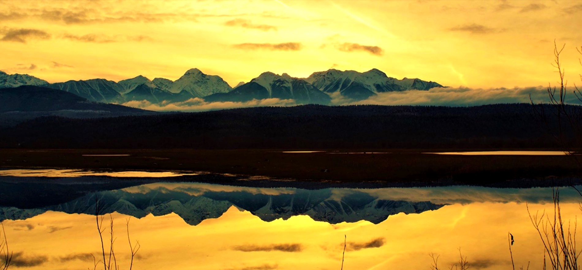 Golden sunset reflected in still water below the peaks of the Canadian Rockies
