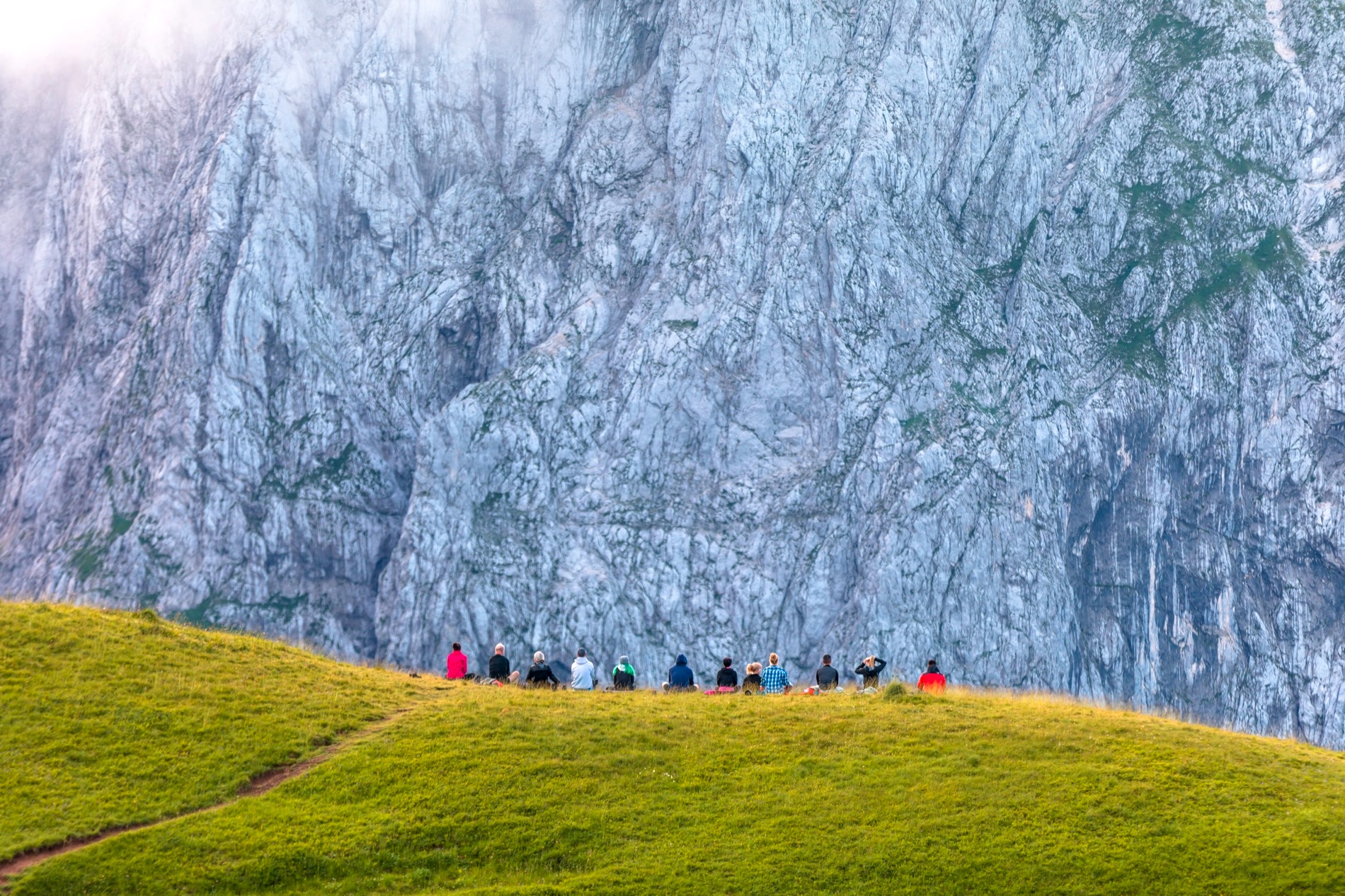 A group practising yoga on a mountain meadow below a limestone face, Julian Alps